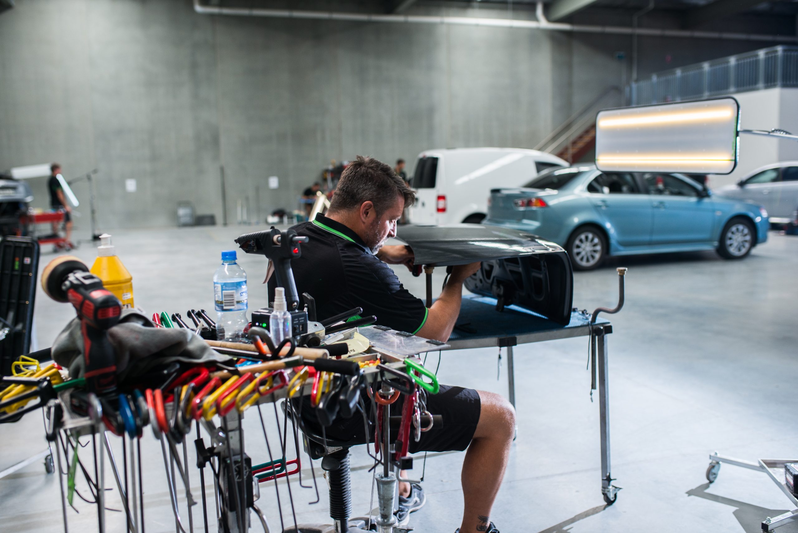 A UHR specialist carrying out paintless dent repairs under an inspection light