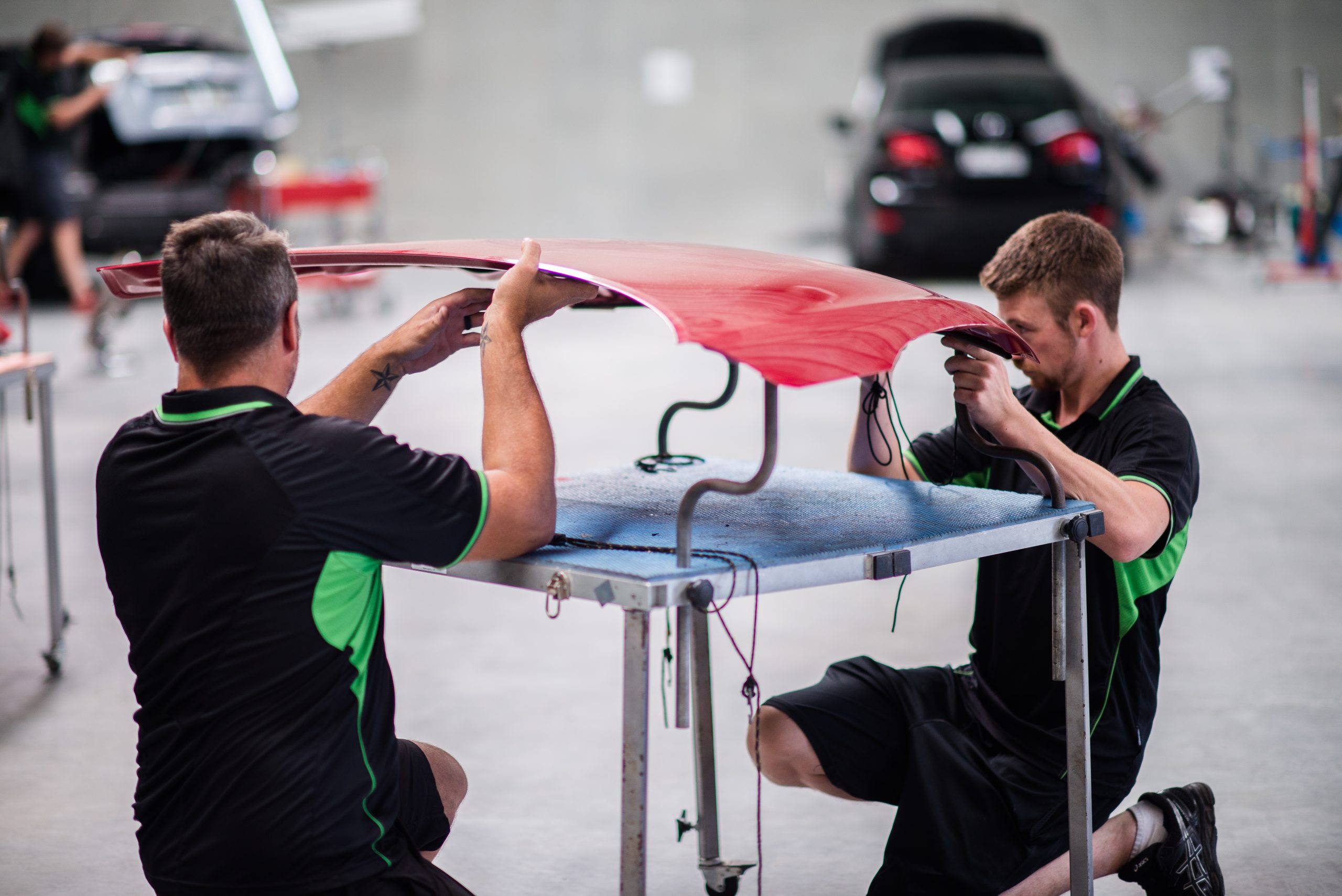 Two UHR technicians carefully repairing a red vehicle bonnet in the workshop